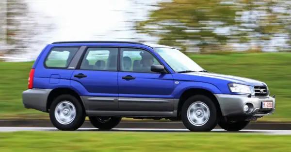 Niebieskie auto 4x4 Subaru Forester z napędem na cztery koła pędzi po drodze, otoczone zielenią.