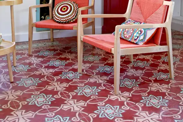 Sol rouge orné de motifs géométriques complexes, typiques des pose carreaux de ciment. Deux fauteuils orange vif avec coussins colorés.