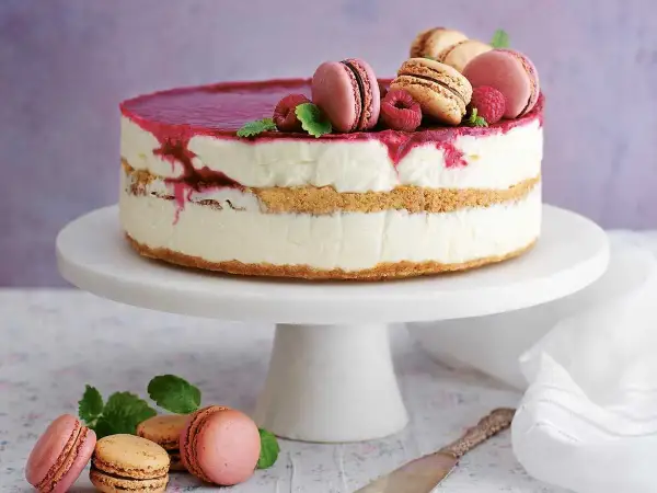 En vacker nyårstårta med lager av krämig fyllning, kexbotten och hallonspegel. Toppad med macarons, hallon och mynta. Ett perfekt nyårstårta recept!