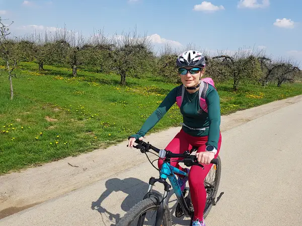 Kobieta na rowerze podziwia sandomierskie trasy rowerowe wśród kwitnących sadów.