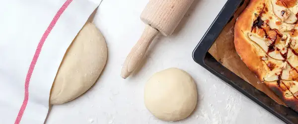 En utbakad pizza med päron och nötter i en form. Bredvid ligger deg och kavel, redo för nästa bak.