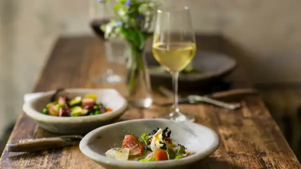 Un bicchiere di vino bianco per cucinare accompagna un pasto raffinato con piatti di pesce e verdure su un tavolo di legno rustico.