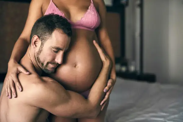 Czuły mężczyzna obejmuje brzuch ciężarnej kobiety. Delikatne pozycje seksualne w ciąży, pełne miłości i bliskości.