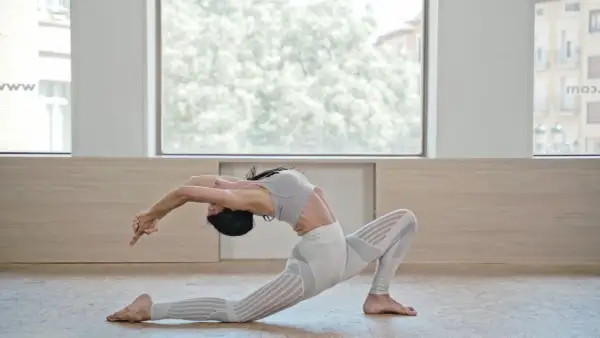Mujer en postura de Anjaneyasana yoga, arqueando la espalda y extendiendo brazos hacia atrás.