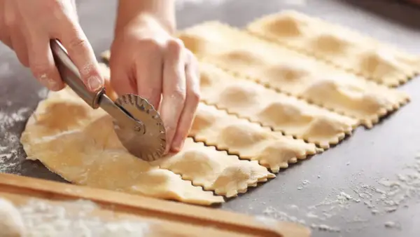 Hände schneiden mit einem Teigrädchen frische Ravioli. So einfach ist ravioli selber machen.