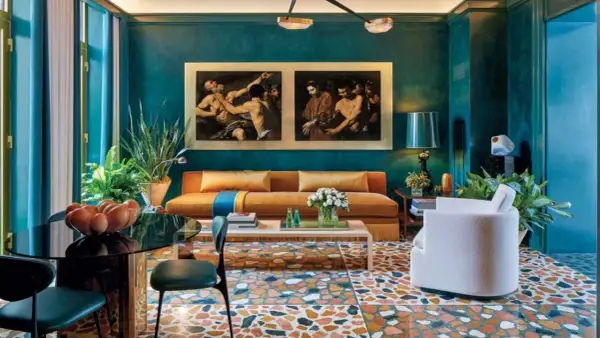 Soggiorno con divano arancione, quadri classici e pavimento a terrazzo. La differenza tra ottanio e petrolio è evidente nei toni del muro e delle tende.