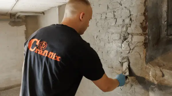 Mann trägt dickbeschichtung bitumen auf eine Ziegelwand auf.