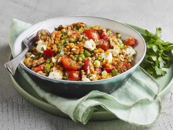 Ein bunter rote Linsen Salat mit Tomaten, Feta und Kräutern, appetitlich in einer Schüssel serviert.