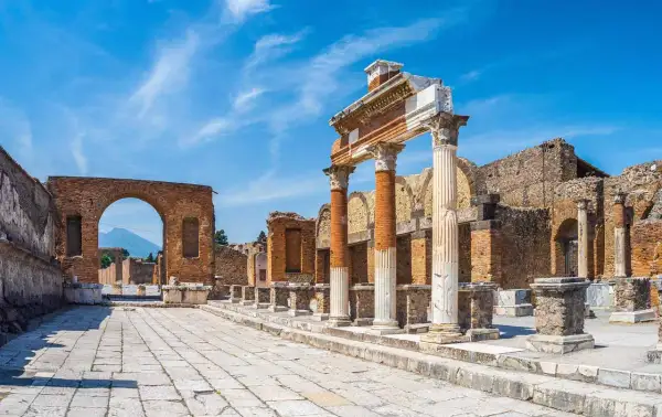 Ruines antiques de Pompéi sous un ciel bleu. Colonnes imposantes et un arc de brique invitent à visiter Pompéi et à imaginer la vie d'autrefois.