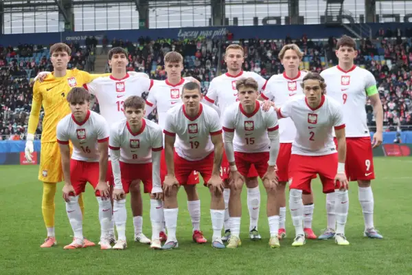 Młoda drużyna piłkarska w biało-czerwonych strojach, gotowa do gry. W tle trybuny stadionu, gdzie kibice dopingują lublin klub piłkarski.