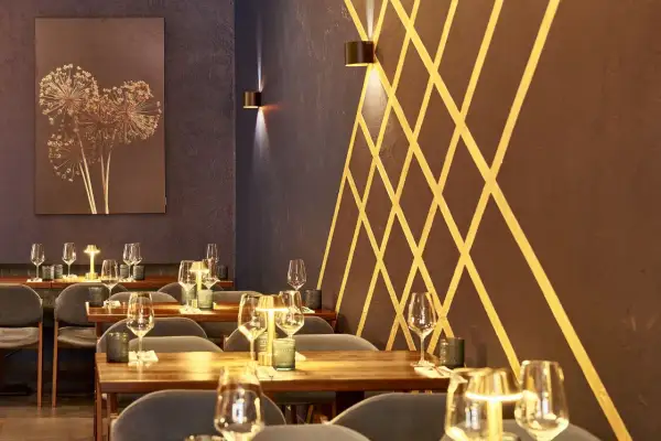 Stilvolles Ambiente im Lovis Restaurant: gedeckte Tische mit Gläsern und Kerzen, dunkle Wände mit goldenem Muster und ein Kunstwerk mit getrockneten Blumen.