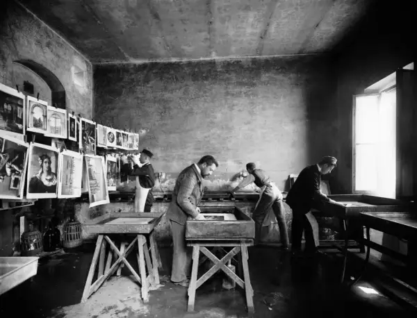 Alessandro Bardi e collaboratori lavorano in un laboratorio di stampa, con stampe appese e vasche per il trattamento.