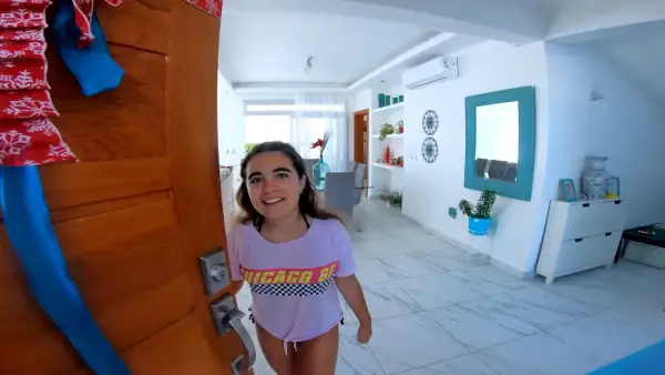 Joven sonriente abre la puerta de su casa, decorada para Navidad, lista para un intercambio de trabajo por alojamiento.