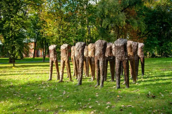 Rzeźby Magdaleny Abakanowicz, grupa bezgłowych postaci, stoi na trawiastym, jesiennym dziedzińcu.