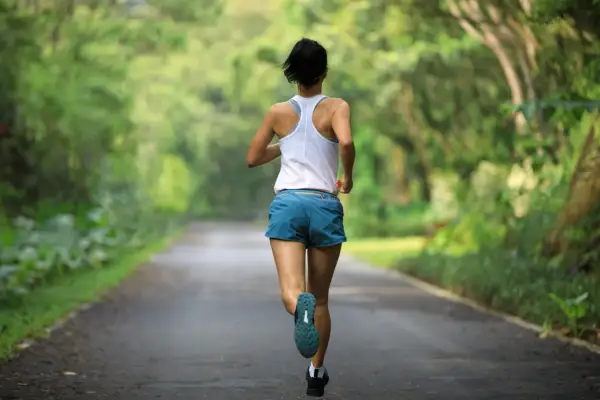 Kobieta biegnie leśną drogą. Czy bieganie to cardio? Zdecydowanie tak! To świetny trening dla serca.