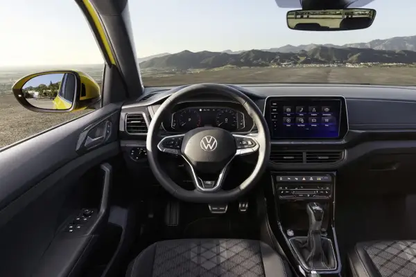 Interni di un'auto Volkswagen con volante, cruscotto digitale e schermo touchscreen. Vista dal posto di guida verso l'esterno.