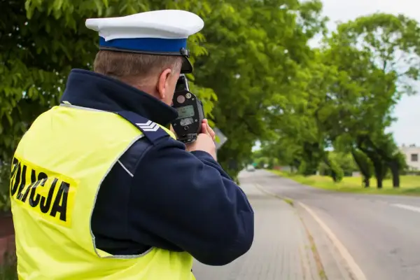 Policjant w kamizelce odblaskowej mierzy prędkość samochodu za pomocą fotoradaru.