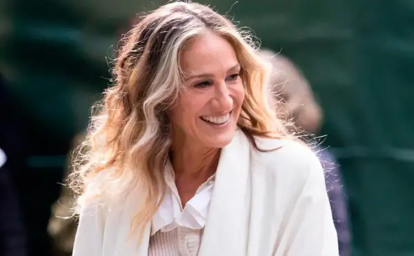 Mujer sonríe con cabello rubio y castaño con técnica reverse balayage, luciendo un abrigo blanco.