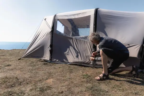 Mężczyzna rozbija namiot na trawiastym klifie nad morzem. Czy można rozbić namiot na plaży? To miejsce wygląda idealnie.