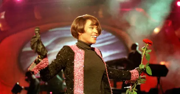 Whitney Houston w Polsce, z mikrofonem i czerwoną różą, w błyszczącej marynarce.