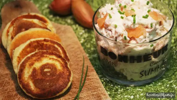 Petits blinis dorés accompagnant un délicieux verre de rillettes de saumon, parsemé de ciboulette fraîche.