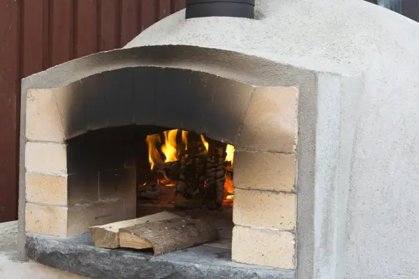 En nybyggd kamin murad med tegel och puts, redo för eldning. Värmen sprider sig från den sprakande elden inuti.