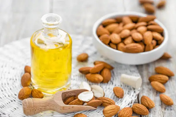 Aceite de almendras en botella, almendras en cuenco y esparcidas. El aceite de almendras mancha la piel con el sol, ¡pero nutre!
