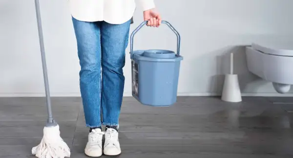 Persona con mocio e secchio pronto per lavare parquet.