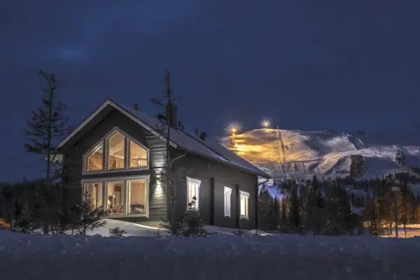 Trillevallen hotell, ett mysigt hus i snölandskap med upplysta skidbackar i bakgrunden.