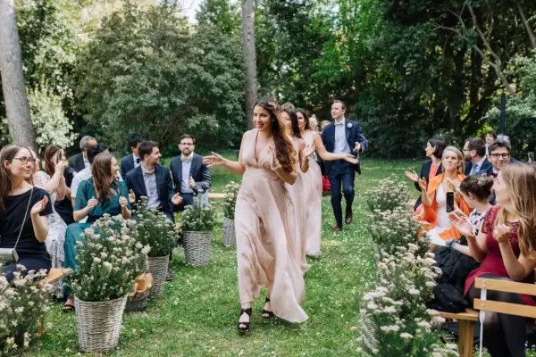 Le cortège d'église pour ce mariage en extérieur est joyeux. Les demoiselles d'honneur, en robes fluides, marchent sur l'herbe, applaudies par les invités.