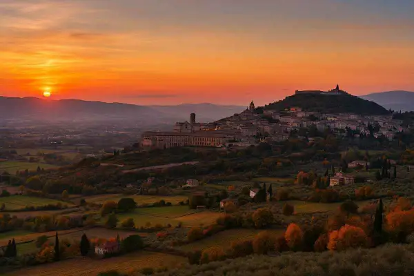 Tramonto infuocato su una città dell'Umbria arroccata su una collina, con uliveti e campi dorati.