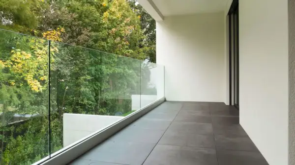 Nowoczesne płytki na balkon w bloku, z widokiem na zielony ogród i szklaną balustradę.