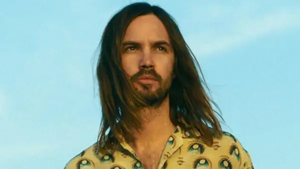 Kevin Parker w koszuli z motywem oczu, z rozwianymi włosami na tle błękitnego nieba.