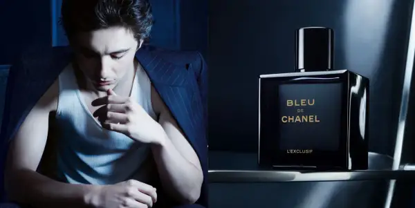 Młody mężczyzna w garniturze i podkoszulku, obok flakonik perfum BLEU DE CHANEL L'EXCLUSIF.