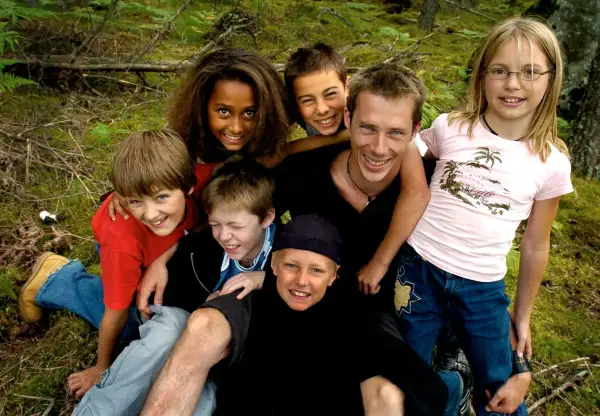 En grupp glada barn och en vuxen njuter av en dag i skogen. De ser ut som riktiga ola wild kids, redo för äventyr.