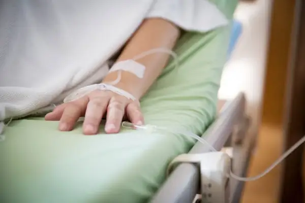 Ręka pacjenta w szpitalnym łóżku z wenflonem, walczącego z infekcją, np. Klebsiella pneumoniae.