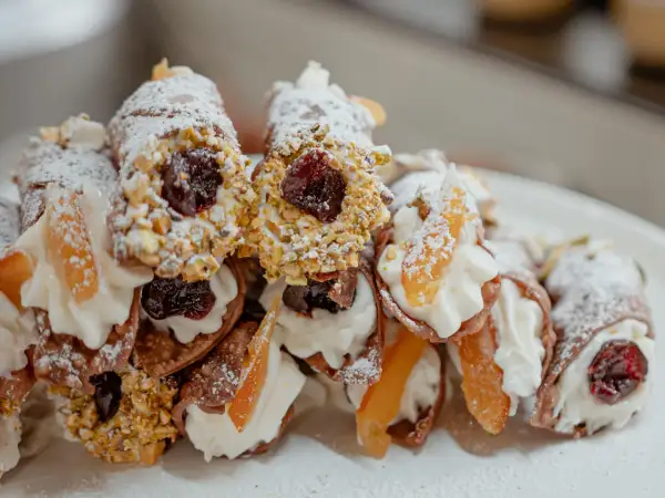 Cannoli garnis avec une généreuse crème de ricotta, des pistaches concassées, des cerises confites et des fruits confits. Saupoudrés de sucre glace.