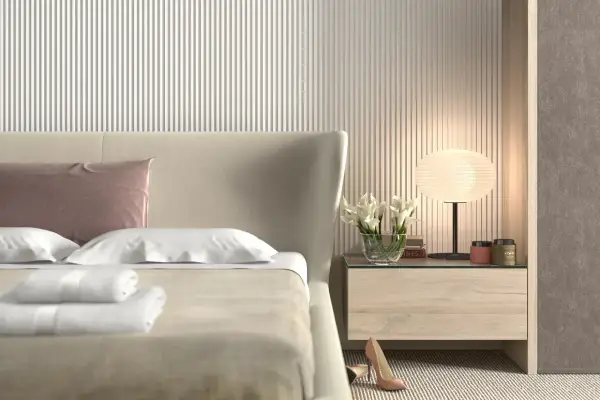 Elegancka sypialnia z łóżkiem, na którym leżą białe ręczniki i różowa poduszka. Ściana za łóżkiem ozdobiona jest pionowymi **lamele w sypialni**.