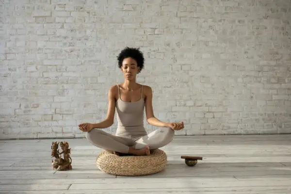 Mujer meditando en postura de loto, con los ojos cerrados y las manos en mudra. A su lado, una figura de bronce y un cuenco tibetano, elementos que invitan a la introspección y a la repetición de **palabras mantra**.