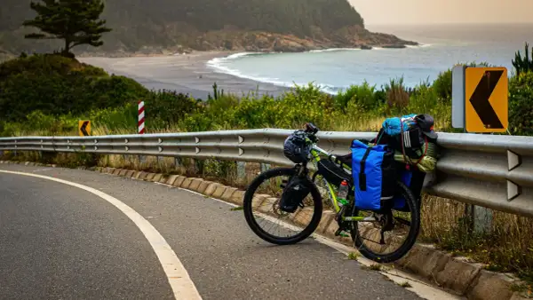 Rower gotowy do bike packingu, obładowany bagażami, stoi przy drodze z widokiem na ocean i plażę.
