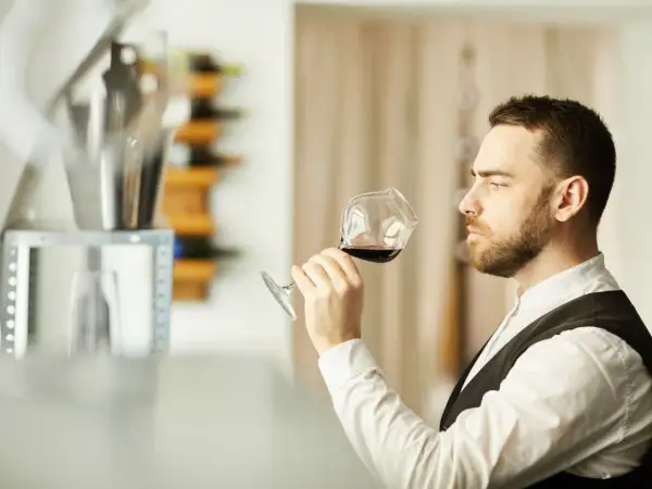 Mężczyzna, degustator win, wącha kieliszek czerwonego wina, oceniając jego aromat.