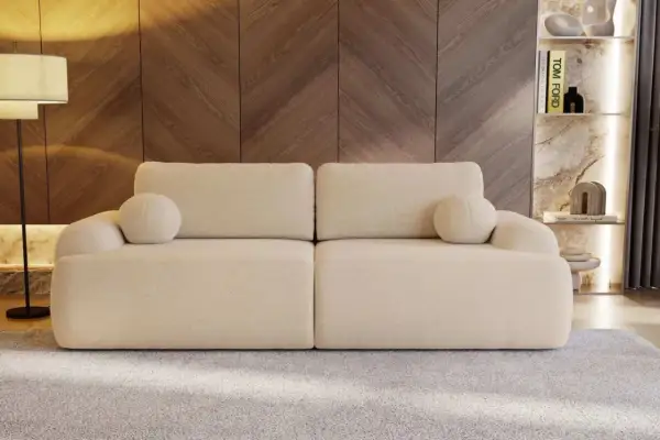 Eine cremefarbene Couch mit runden Kissen, die zum Entspannen einlädt. Sie steht vor einer Holzwand und einem Regal mit Büchern und Deko.