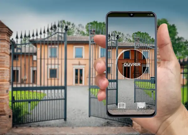 Une main tient un iPhone affichant une application de télécommande universelle pour ouvrir le portail d'une villa.