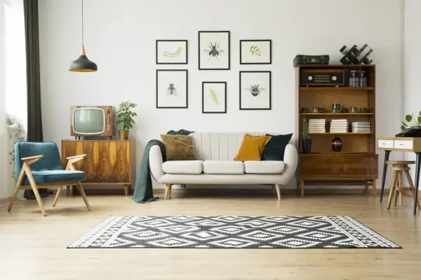 Przytulny salon retro z kanapą, fotelem i meblami z lat 60. Obrazy z owadami i paprociami dodają uroku.