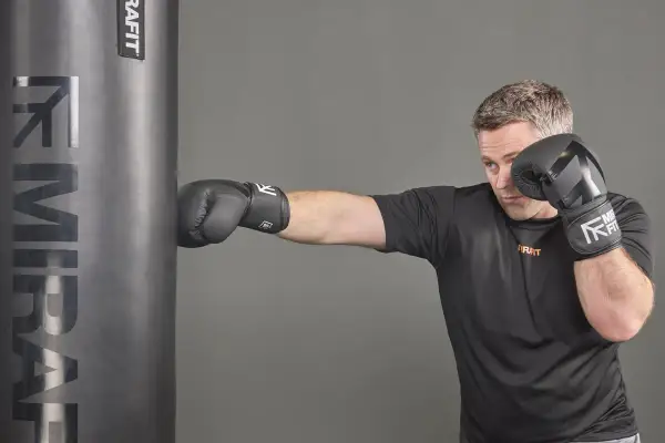 Man in boxing gloves punches a heavy bag, showcasing the full-body workout and the muscles boxing works.