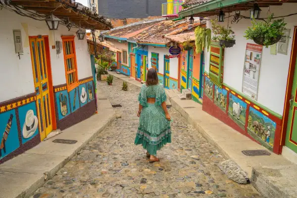 Una mujer camina por una calle empedrada entre casas coloridas, un ejemplo vibrante de los pueblos de Colombia.