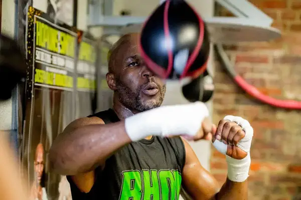 A young Bernard Hopkins, sweat glistening, trains intensely with a speed bag in a boxing gym.