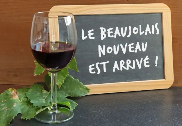 Kieliszek czerwonego wina i tablica z napisem "Le Beaujolais Nouveau est arrivé!" – to znak, że nadszedł czas na święto młodego wina.