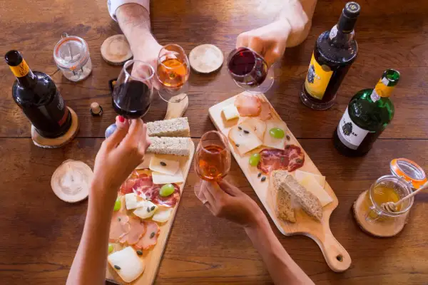 Hände reichen sich Gläser mit Portwein, dazu gibt es Brot, Käse und Aufschnitt. Was ist Portwein? Ein süßer, aufgespriteter Wein aus Portugal.