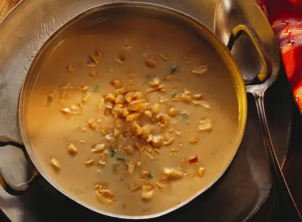 Aksamitna zupa orzechowa, posypana chrupiącymi orzeszkami ziemnymi, w metalowej misie. Obok łyżka i czerwony ręcznik.